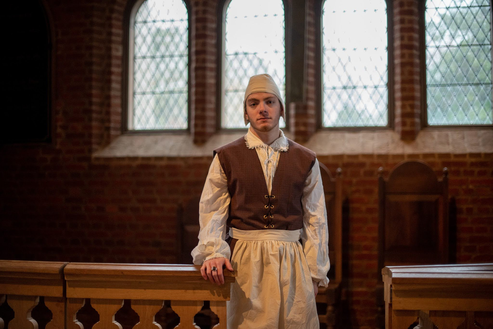 Aubrey stands tall in a sunlit church in Thomas/ine's clothes, somber, with one hand resting on the pews