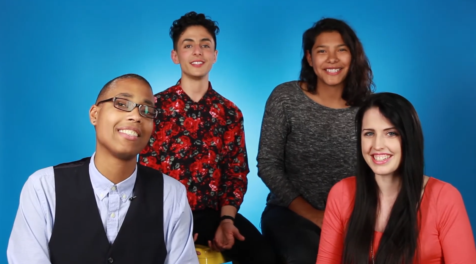 Saifa, Pidgeon, Alice, and Emily sitting together against a bright blue studio background