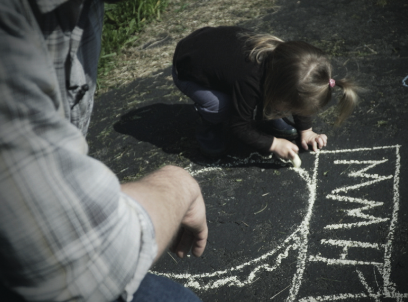 Cover image from the report, a small child with face down playing outside, drawing on the sidewalk with chalk as a parent watches