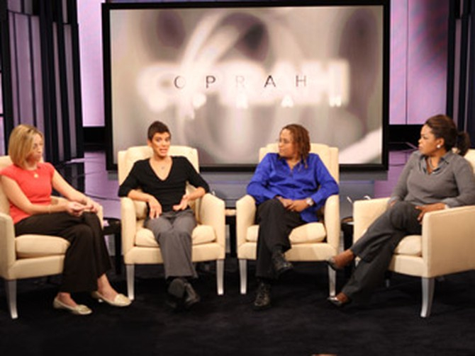 Katie, Hida, and Lynnell sitting in plush chairs on stage, with Oprah to their right