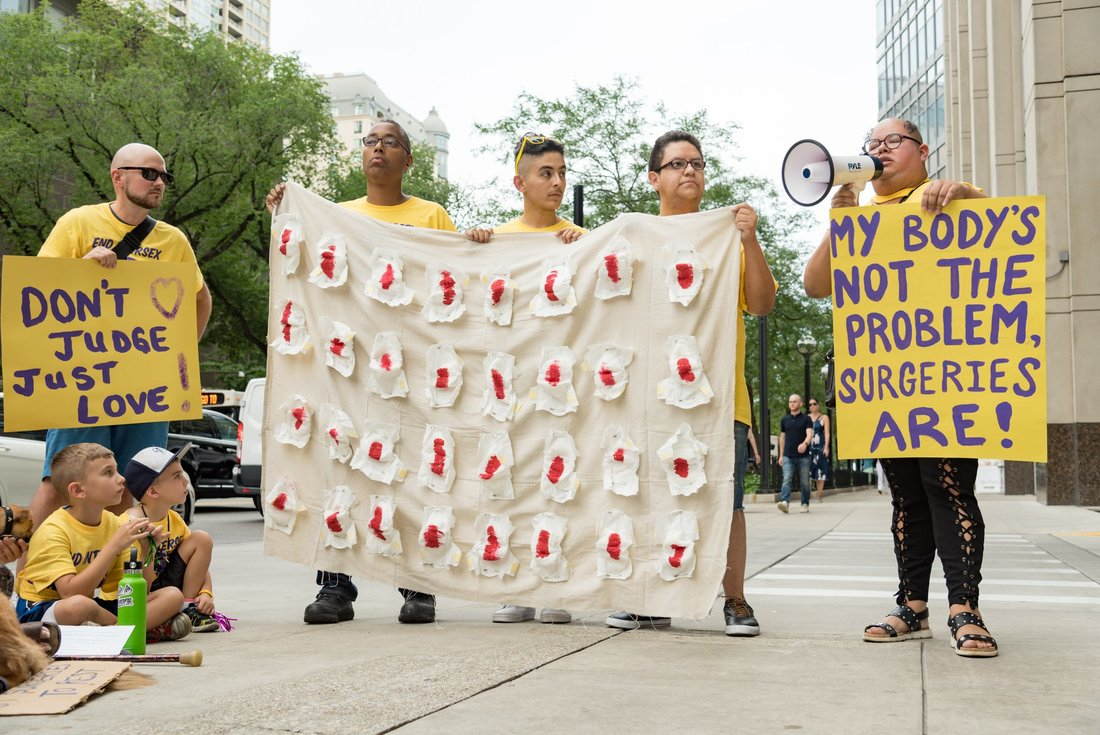 Intersex Justice Project's Chicago protest, with The Houston Intersex Society, holding a banner and art piece. The art piece is Koomah's, a spread of four rows of diapers opened to show blood inside.