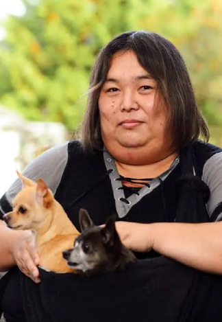 Photo of Emi Koyama, a Japanese-American intersex person with shoulder-length black hair, seated and holding two chihuahuas in her lap