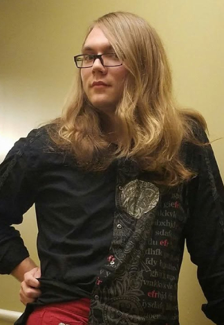 Scout, a white intersex person with shoulder-length blonde hair and glasses, wearing a black dress shirt and bright red pants, looking away with one hand on their hip